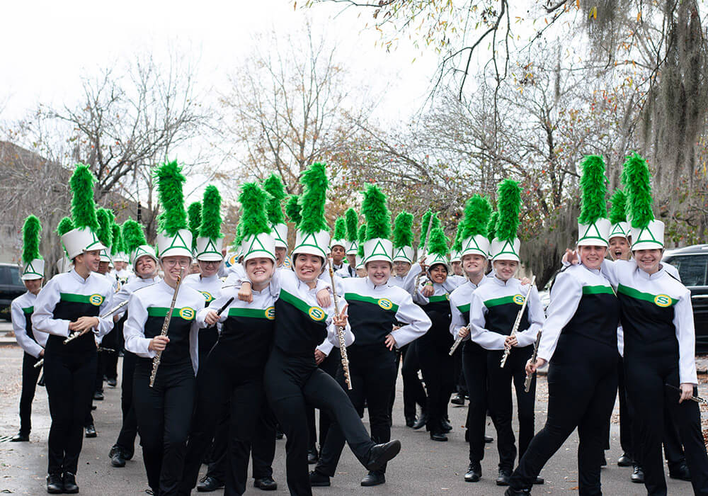A marching band in green and white plumed hats performs along the parade route