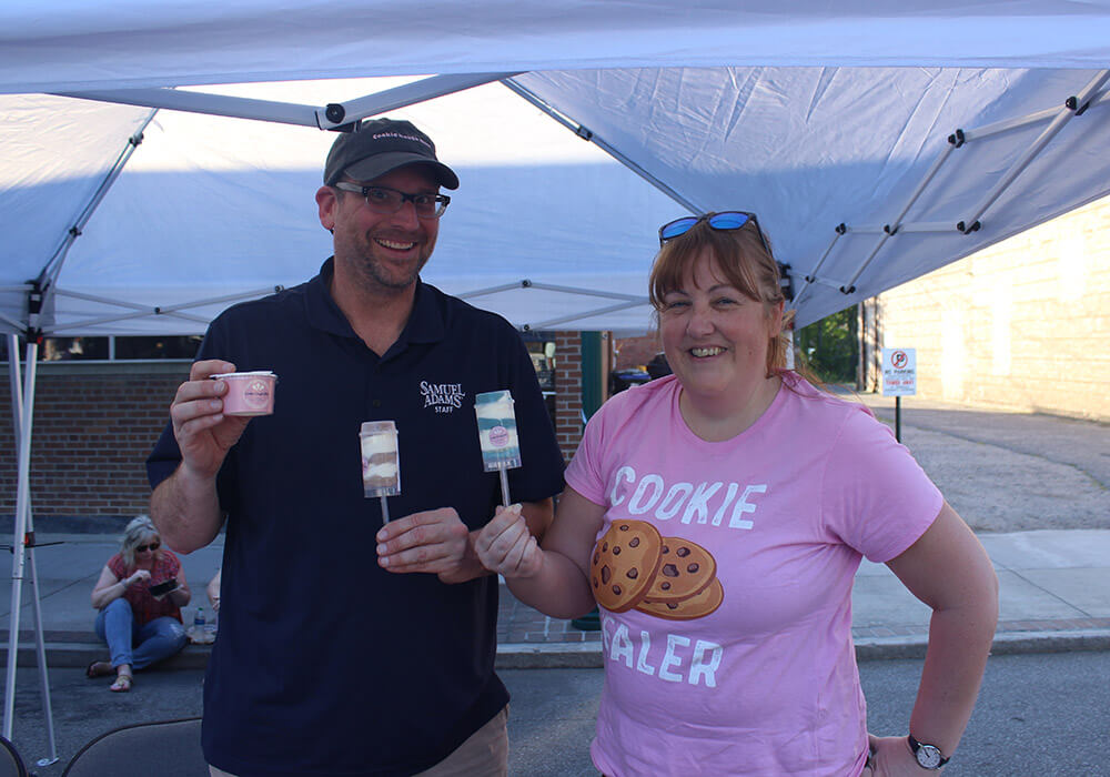 Two vendors smile while holding dessert cups at their tent