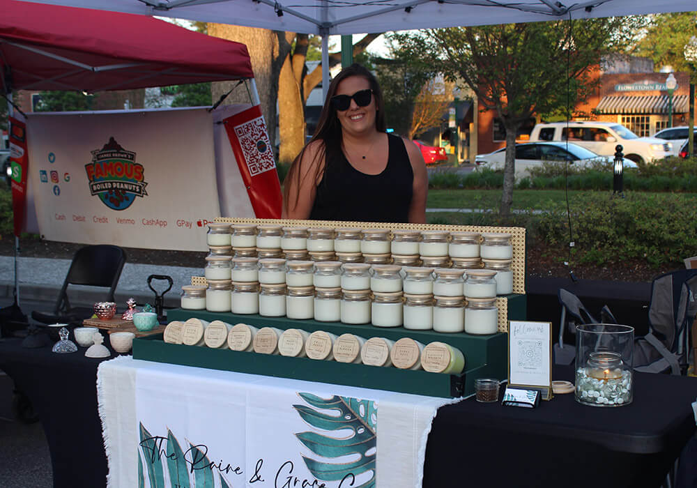 A maker stands behind rows of hand-poured candles at her booth