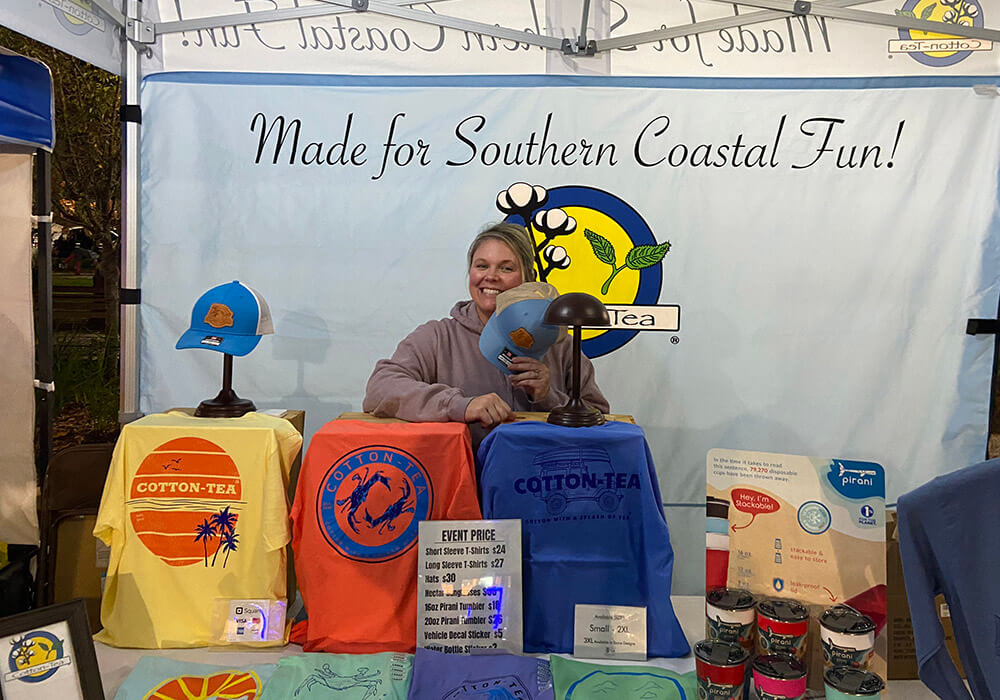 A vendor displays printed T-shirts and tumblers at her booth