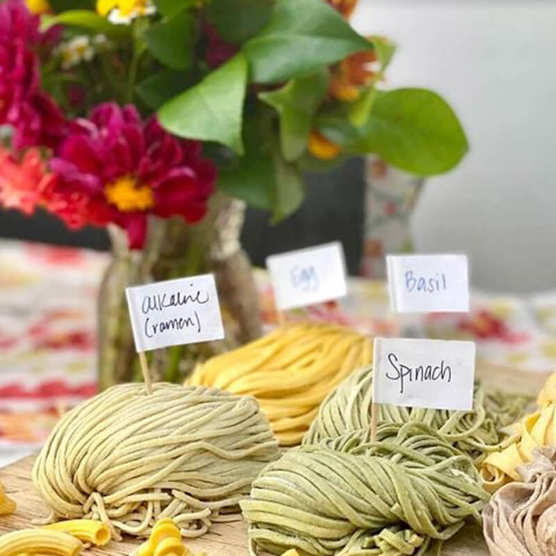 Nests of fresh pasta labelled basil, spinach and egg beside a jar of zinnias